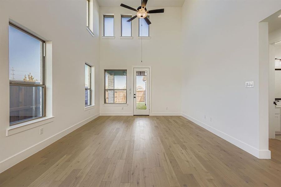 Unfurnished living room with light wood finished floors, a ceiling fan, and a towering ceiling