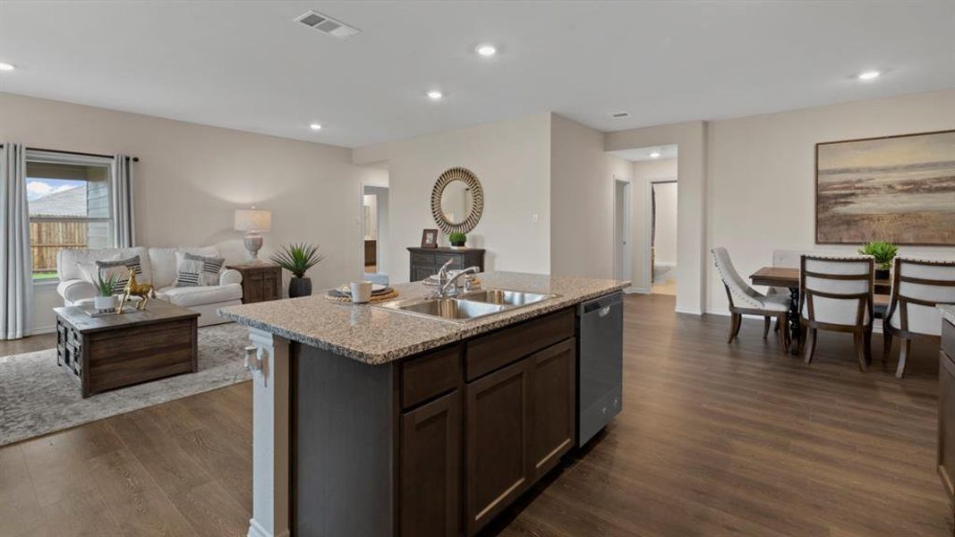 Kitchen featuring open floor plan, a kitchen island with sink, dark wood finish cabinetry, light stone countertops, and stainless steel dishwasher