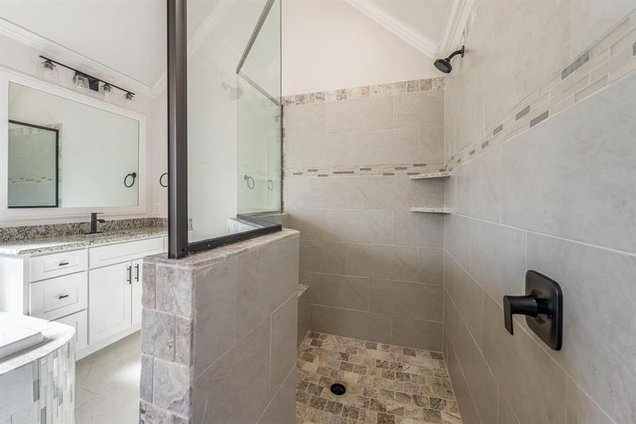 Bathroom featuring a tile shower, vanity, and crown molding