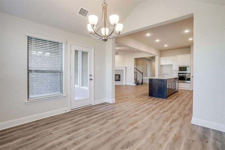 Kitchen with appliances with stainless steel finishes, light hardwood / wood-style flooring, white cabinetry, hanging light fixtures, and an island with sink