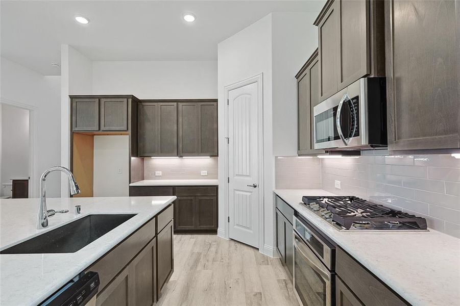 Kitchen featuring decorative backsplash, light hardwood / wood-style flooring, light stone counters, sink, and stainless steel appliances