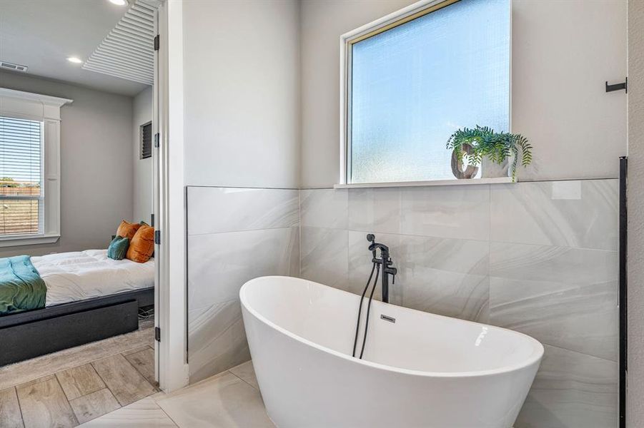Full bathroom with a soaking tub, healthy amount of natural light, tile walls, and wood finished floors