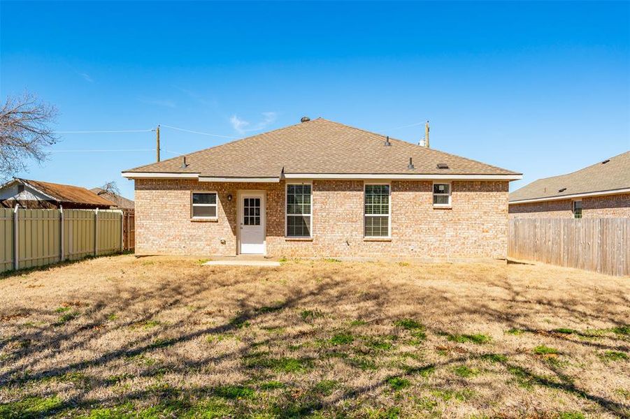 Back of property featuring brick siding, a lawn, a shingled roof, and a fenced backyard