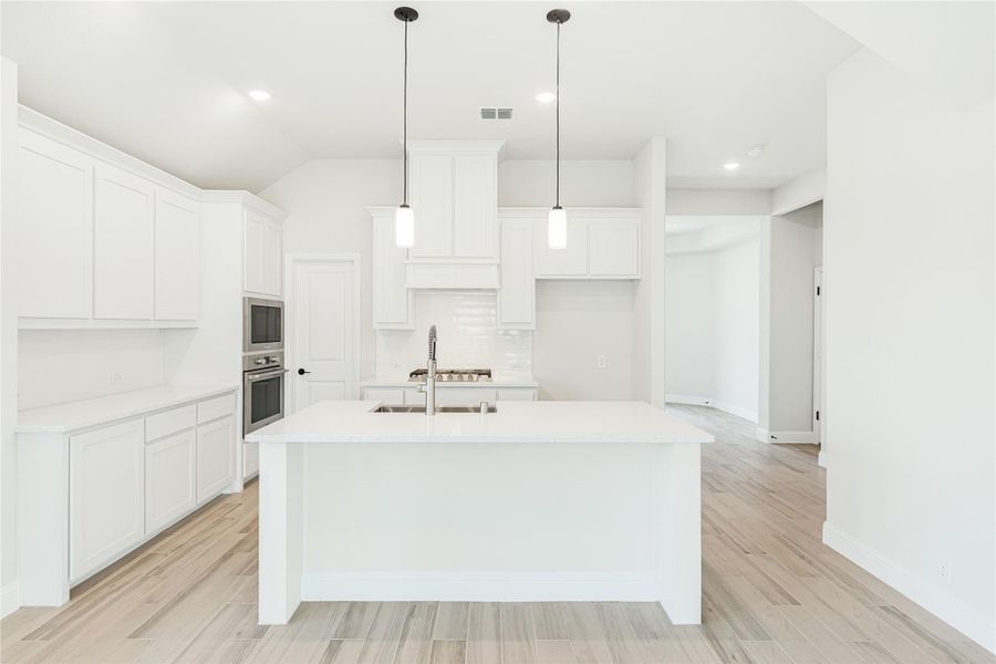 White kitchen with large center island, pendant lights, double wall ovens, and light wood floors