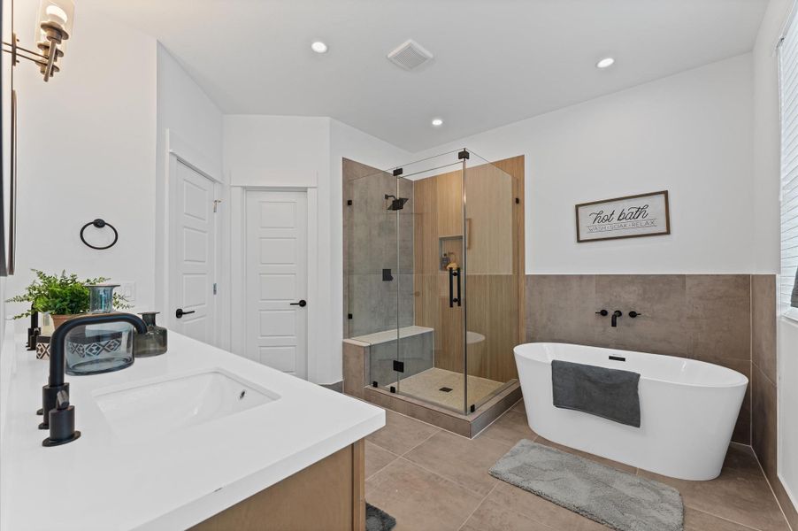 This luxurious primary bathroom blends modern elegance with spa-like comfort, featuring a spacious layout and contemporary selections throughout. A sleek double vanity with minimalist cabinetry and quartz countertops offers ample storage and style, while the glass-enclosed shower includes a built-in bench for added relaxation and convenience. The centerpiece is a sculptural freestanding soaking tub, perfectly positioned to invite unwinding after a long day.