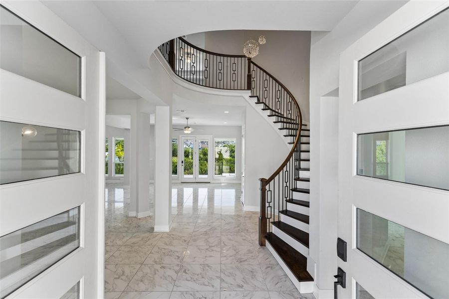 A grand, curved staircase with ornate ironwork anchors the entry, inviting residents into the open-concept living areas.