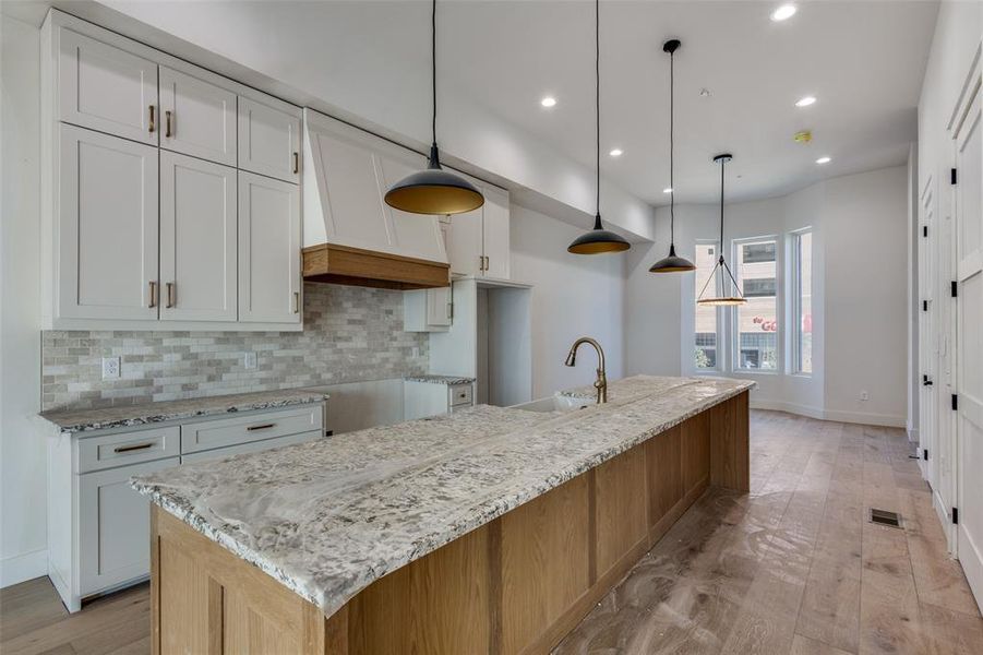 Kitchen featuring white cabinets, a spacious island, and decorative light fixtures. This Home is under constructions and not the property for sale representative of finish out in #110.