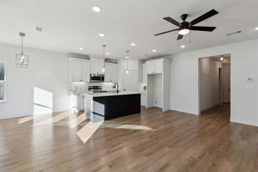 Kitchen featuring white cabinets, appliances with stainless steel finishes, a center island with sink, and pendant lighting