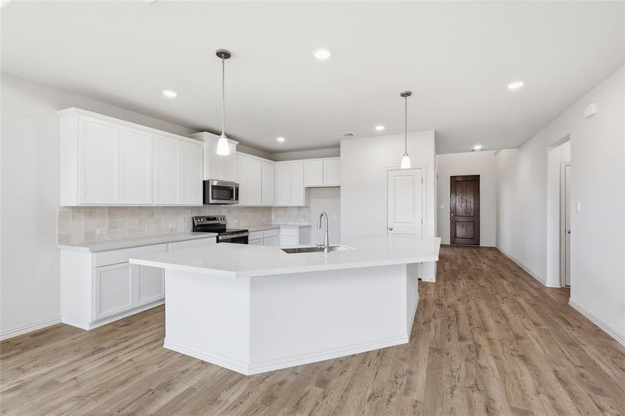 Modern kitchen featuring a large central island with a sink, white cabinetry, integrated stainless steel appliances, and wood-finish flooring