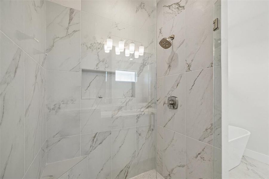 Walk-in shower featuring large format marbled tile, a built-in shower niche, and a rain showerhead