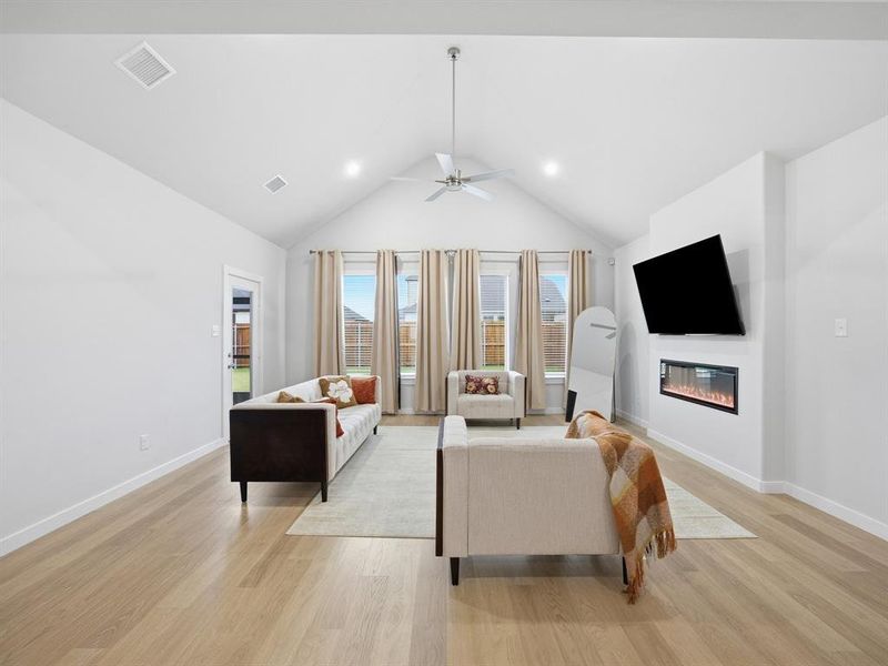 Living area with light wood-style floors, a glass covered fireplace, high vaulted ceiling, ceiling fan, and recessed lighting