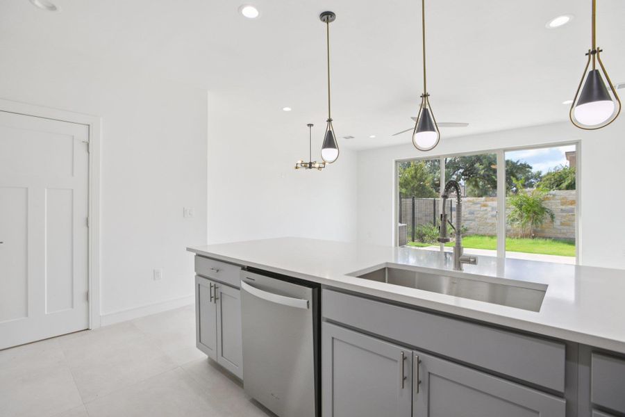 Kitchen with stainless steel dishwasher, gray cabinetry, pendant lighting, and light stone countertops