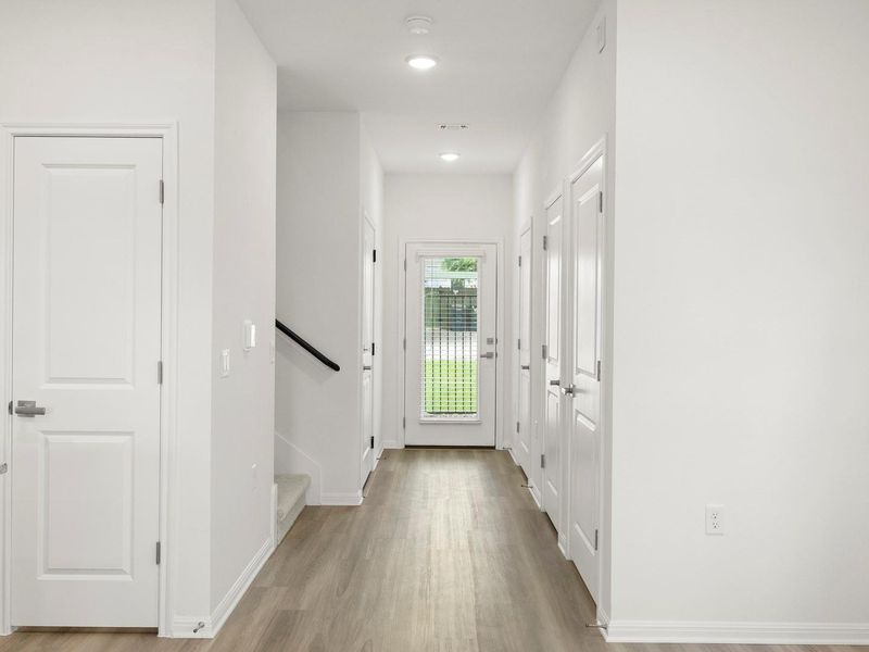 A well-lit hallway with durable wood-style flooring extends toward an inviting entry door.