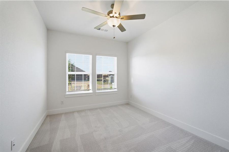 Bright room featuring two windows with blinds, light gray patterned carpet, white walls, and a ceiling fan with integrated lighting Bright room featuring two windows with blinds, light gray patterned carpet, white walls, and a ceiling fan with integrated lighting