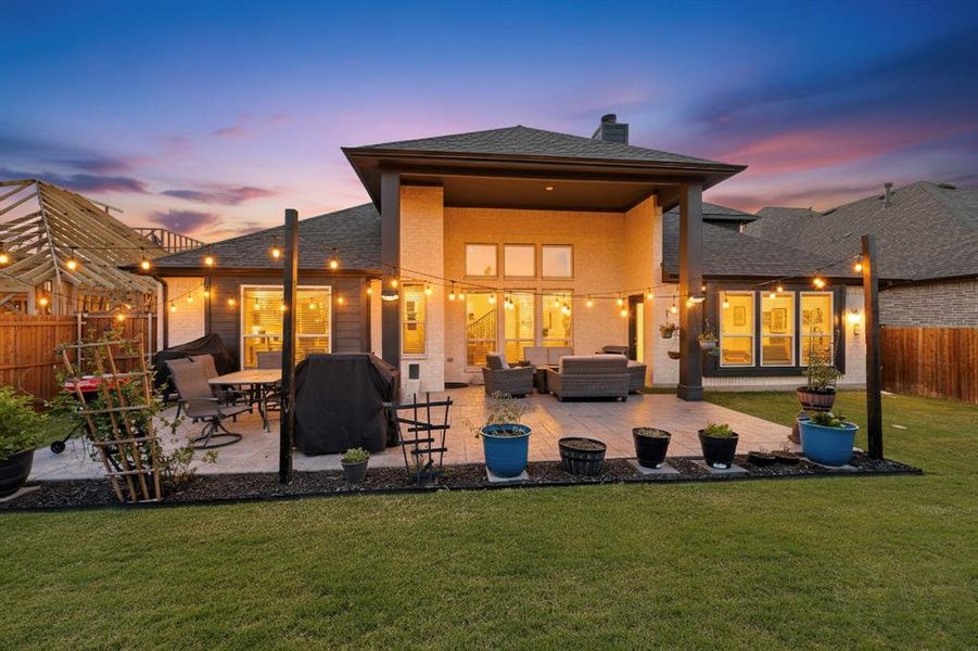 Back of house at dusk with brick siding, a chimney, a shingled roof, and a patio area Back of house at dusk with brick siding, a chimney, a shingled roof, and a patio area
