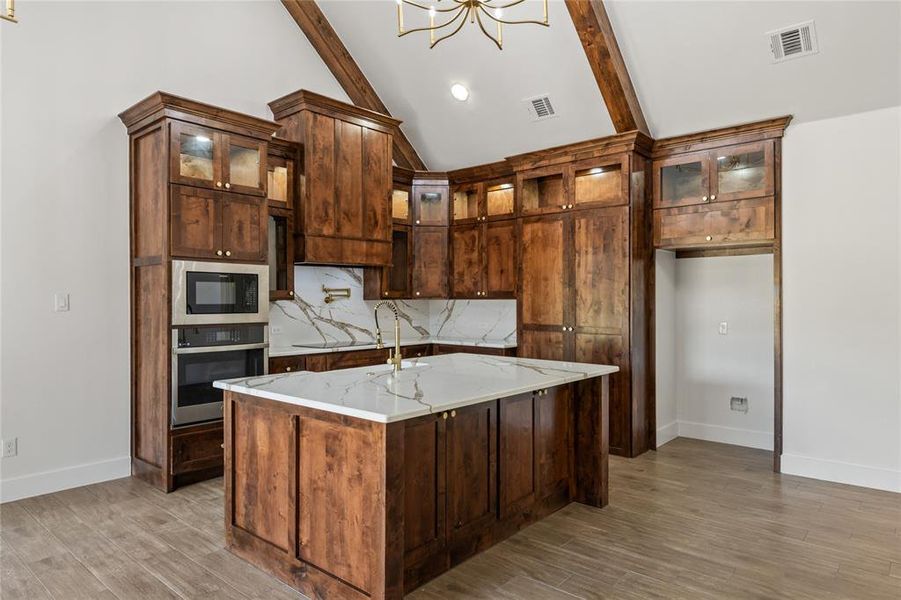 Kitchen featuring stainless steel appliances, light stone counters, light wood-type flooring, glass insert cabinets, and vaulted ceiling