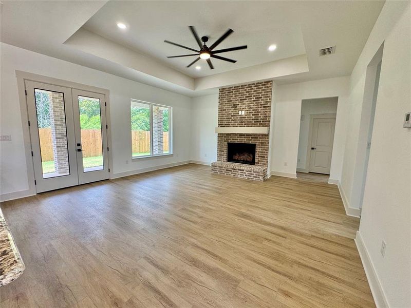 Unfurnished living room with a raised ceiling, a fireplace, light wood-type flooring, french doors, and recessed lighting