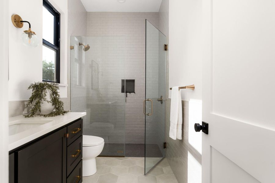 A well-lit bathroom features a glass-enclosed shower and a modern vanity with contrasting dark cabinetry.
