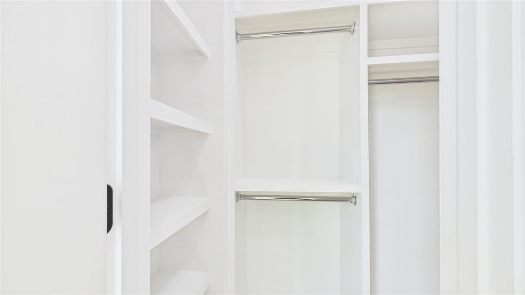 This photo shows a well-organized, spacious white closet with multiple shelves and double hanging rods, providing ample storage space.