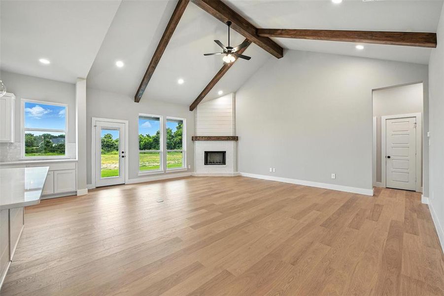 Unfurnished living room featuring beam ceiling, recessed lighting, light wood-style flooring, a large fireplace, and high vaulted ceiling Unfurnished living room featuring beam ceiling, recessed lighting, light wood-style flooring, a large fireplace, and high vaulted ceiling