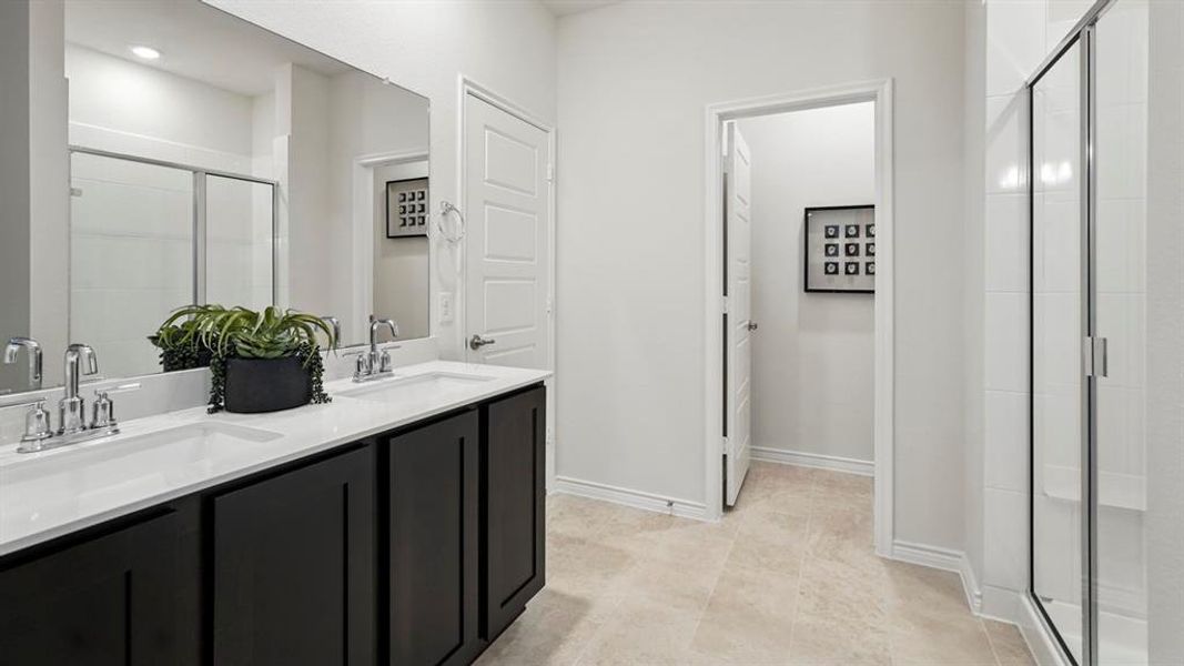 Bathroom featuring a shower stall, double vanity, and light tile patterned floors
