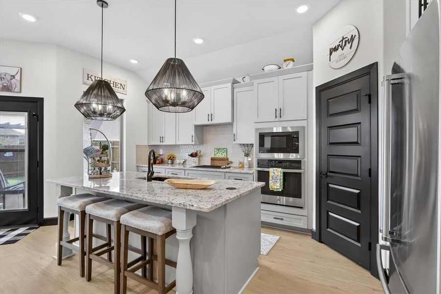 Kitchen featuring a granite-topped island with seating, stainless steel appliances, light cabinetry with dark hardware, and wood-finish flooring