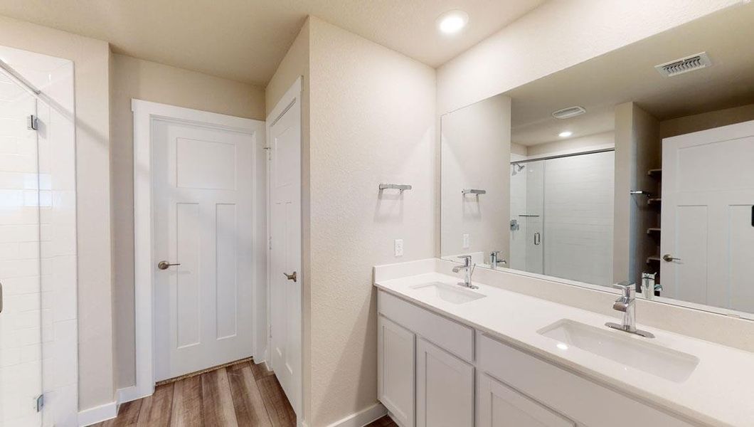 Full bathroom featuring double vanity, light wood-style floors, a stall shower, and a closet