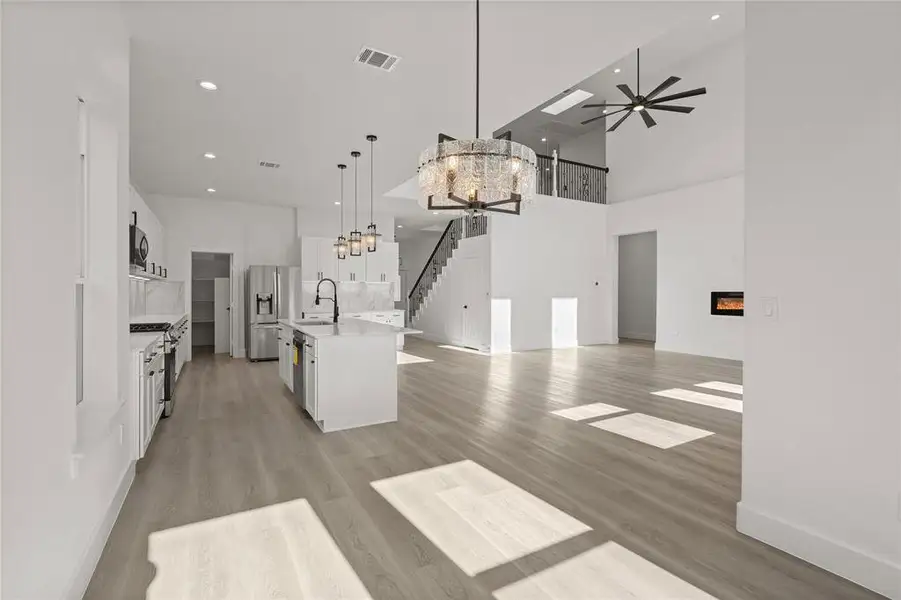 Kitchen featuring white cabinets, a glass covered fireplace, a chandelier, a high ceiling, and light wood-style flooring