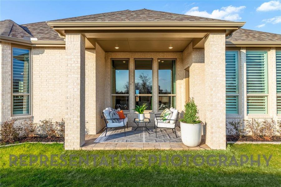 Property entrance with brick siding, a patio area, a shingled roof, and a yard Property entrance with brick siding, a patio area, a shingled roof, and a yard