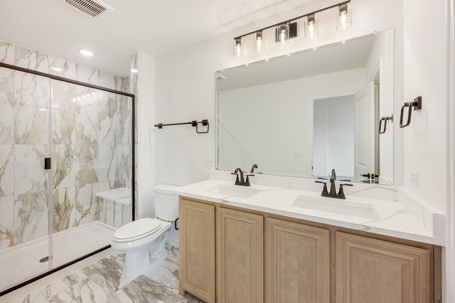 Bathroom with double sink vanity, marble tile shower with glass door, and white countertops Bathroom with double sink vanity, marble tile shower with glass door, and white countertops