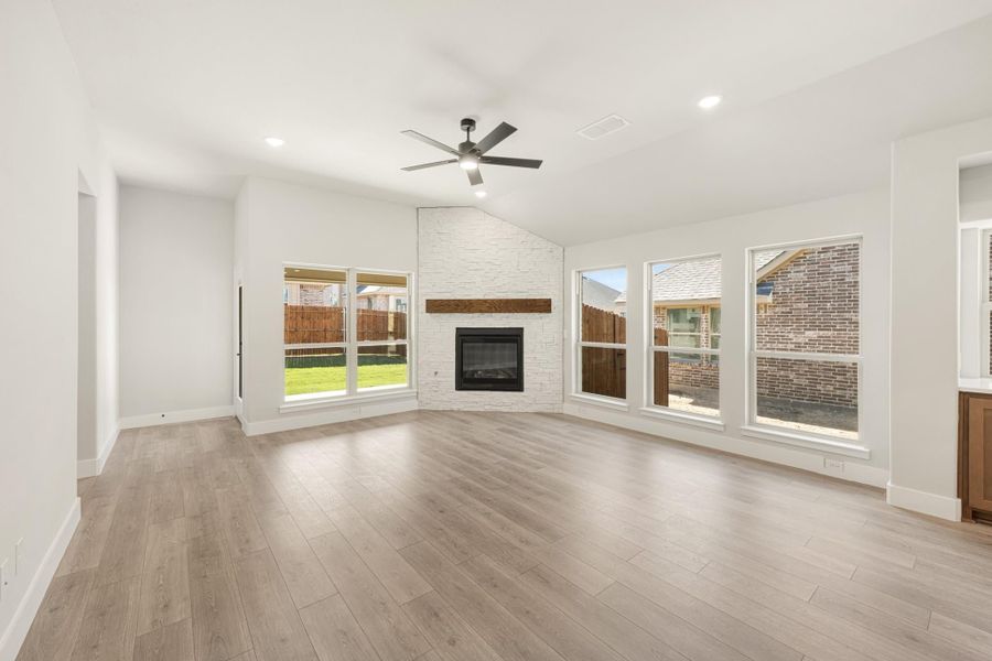 Open living room with wood floors, white stone fireplace, ceiling fan, and large windows Open living room with wood floors, white stone fireplace, ceiling fan, and large windows
