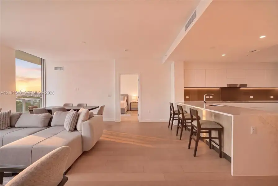 Open-concept interior featuring light wood-finish flooring, a kitchen with flat-panel cabinetry, a waterfall-edge countertop island, and recessed ceiling lighting