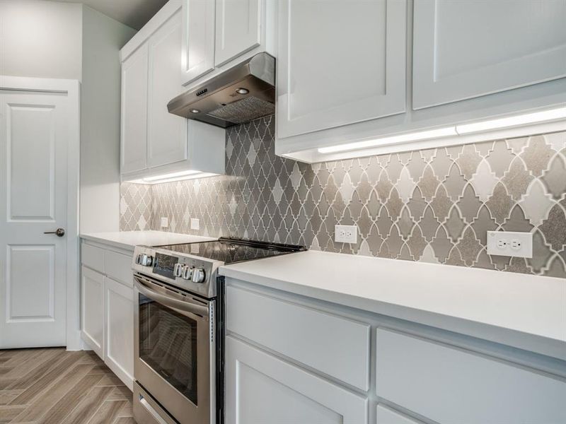 Kitchen with under cabinet range hood, backsplash, light countertops, and electric stove