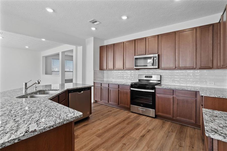 This kitchen will not disappoint! Your family and guests will enjoy many nights of fun, food and entertainment with ample counter space and kitchen island for setting up a wonderful array of provisions! This view of this gorgeous kitchen showcases SS appliances, granite countertops, beautiful tile backsplash, gas range, high ceiling, recessed lighting and tile floors!