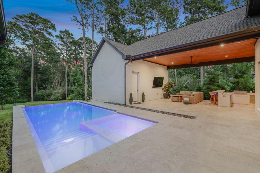 Resort-style outdoor living at its finest! This stunning backyard is designed for both relaxation and entertaining, featuring a sleek modern pool with a sun shelf and spa, all surrounded by elegant natural stone decking. The expansive covered terrace boasts a warm wood-paneled ceiling, recessed lighting, ceiling fan, outdoor television, and a fully equipped outdoor kitchen with bar seating. Enjoy seamless indoor-outdoor living while overlooking a private, wooded backdrop with no rear neighbors!