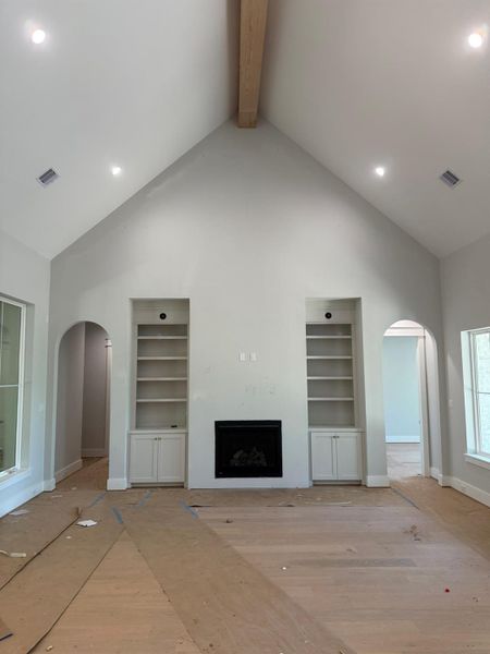 Unfurnished living room with arched walkways, high vaulted ceiling, built in shelves, a fireplace, and beam ceiling