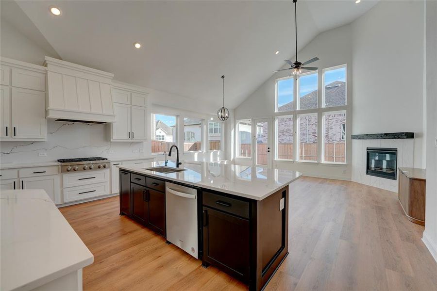 Kitchen featuring vinyl flooring, appliances with stainless steel finishes, a kitchen island with sink, a sink, and a tile fireplace