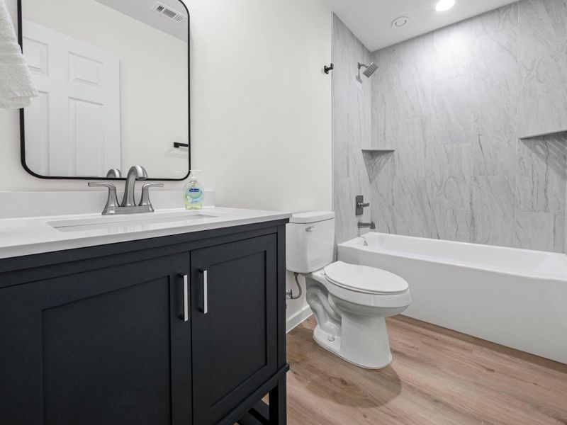 Bathroom featuring a dark vanity with a white countertop, coordinating rectangular mirror, and a full bathtub with tiled surround