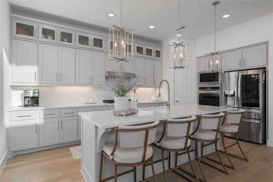 Kitchen featuring light wood finished floors, tasteful backsplash, a center island with sink, appliances with stainless steel finishes, and light countertops