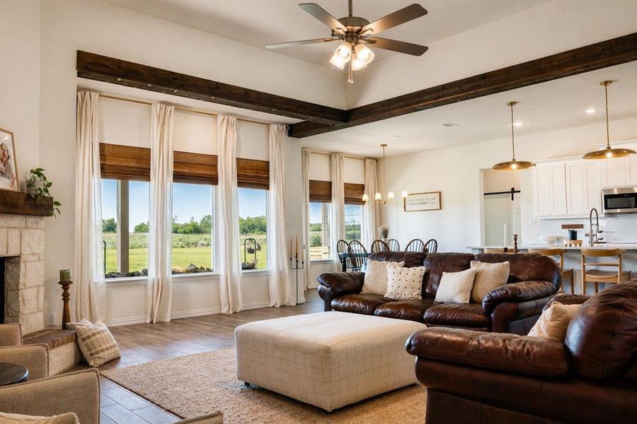 Spacious living area featuring exposed wood beams, a stone-clad fireplace, and large windows with natural light