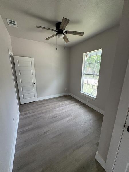 Neutral-toned interior featuring wood-finish flooring, a ceiling fan with light, and a paneled door Neutral-toned interior featuring wood-finish flooring, a ceiling fan with light, and a paneled door