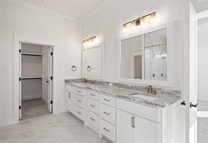 Full bath featuring double vanity, a stall shower, ornamental molding, and light marble finish floors