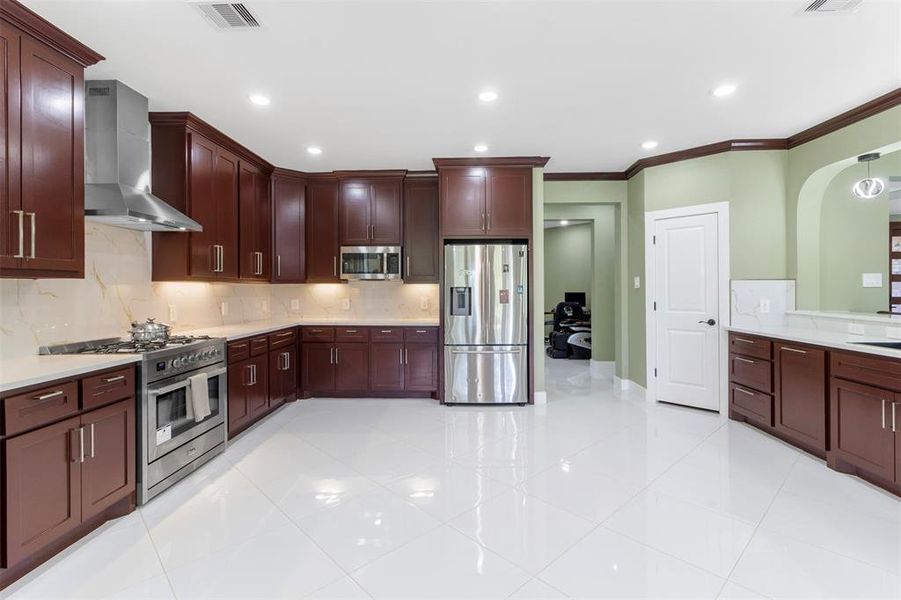 Spacious kitchen with sleek dark wood cabinets, modern stainless steel appliances, and polished countertops. The room is well-lit with recessed lighting and features a clean, open layout with light-colored tile flooring.