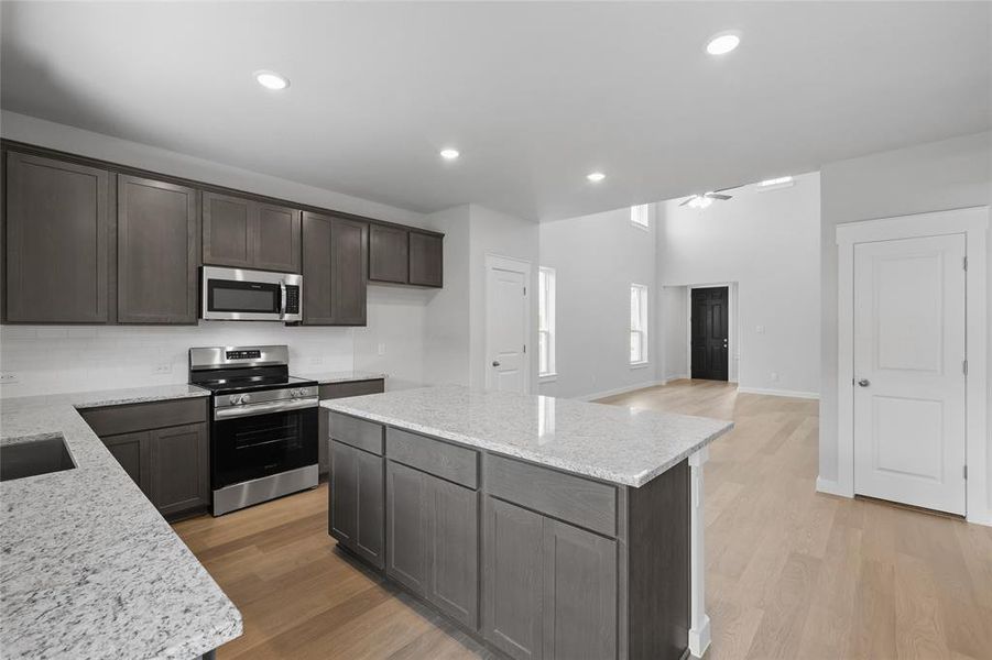 Kitchen with stainless steel appliances, light stone countertops, a center island, dark wood finish cabinets, and light wood finished floors