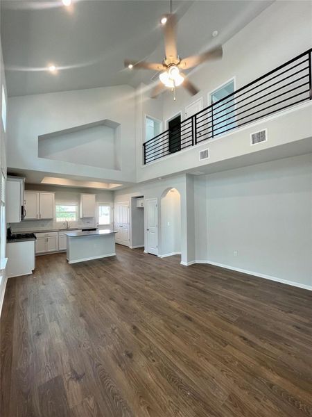 Experience modern elegance in this expansive living room featuring soaring ceilings, sleek Rev Wood floors, and an open layout seamlessly connecting to a stylish kitchen, perfect for entertaining and everyday comfort.