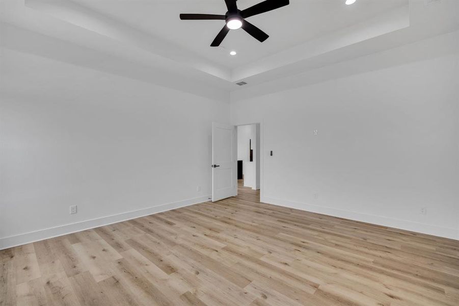 Unfurnished room with light hardwood / wood-style flooring, ceiling fan, and a raised ceiling