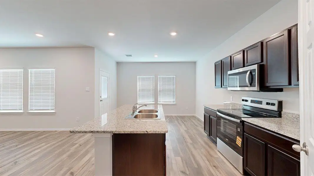 Kitchen featuring dark brown cabinetry, appliances with stainless steel finishes, a center island with sink, light stone counters, and recessed lighting Kitchen featuring dark brown cabinetry, appliances with stainless steel finishes, a center island with sink, light stone counters, and recessed lighting