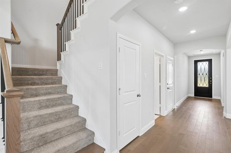 Entryway featuring wood-finish flooring, a carpeted staircase with wood handrails, a decorative front door with leaded glass, recessed lighting, and white paneled doors Entryway featuring wood-finish flooring, a carpeted staircase with wood handrails, a decorative front door with leaded glass, recessed lighting, and white paneled doors