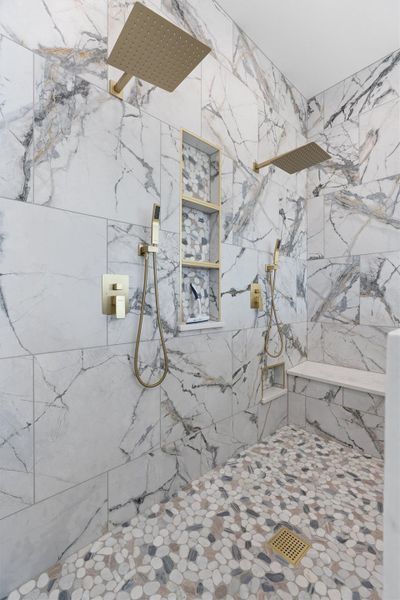 A spacious shower with dual rain heads, handheld sprayers, and marble-patterned tile, complemented by a pebble mosaic floor. A spacious shower with dual rain heads, handheld sprayers, and marble-patterned tile, complemented by a pebble mosaic floor.