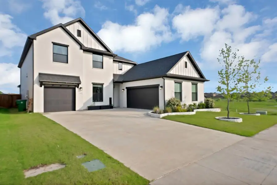 Contemporary two-story residence featuring a white stucco exterior with dark trim accents, a dark shingle roof, and a prominent board-and-batten gable Contemporary two-story residence featuring a white stucco exterior with dark trim accents, a dark shingle roof, and a prominent board-and-batten gable